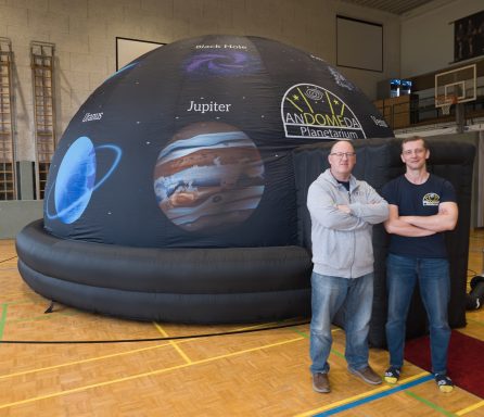 Zwei Personen stehen neben einem aufblasbaren Planetarium mit Planetenabbildungen.